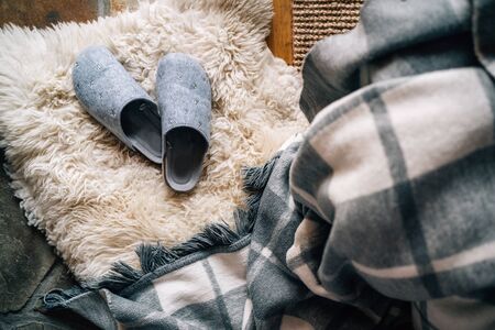 The pair of gray home slippers near the  bed on the white sheepskin in the cozy bedroom. Home sweet home concept top view image.の写真素材