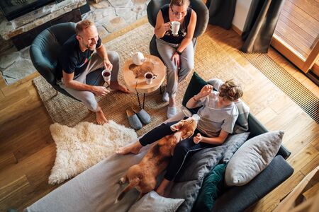 Cozy family tea time. Father, mother and son  at the home living room. Boy lying in comfortable sofa and  stroking their beagle dog and smiling. Peaceful family moments concept image.の写真素材