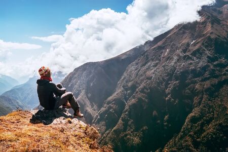 Young female hiker backpacker sitting on the peak edge and enjoying mountains viewの写真素材