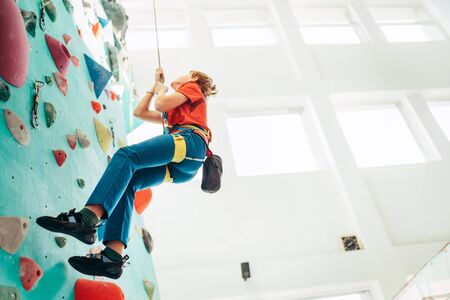 Teenager boy at indoor climbing wall hall. Boy is climbing using a top rope,chalk bag and climbing harness. Active teenager time spending concept image.の写真素材