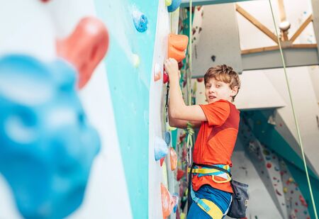 Smiling teenager boy at indoor climbing wall hall. Boy is climbing using a top rope,chalk bag and climbing harness. Active teenager time spending concept image.の写真素材