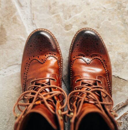 A pair of Brown natural leather medium boots with unlaced shoelaces standing on natural stone floor top view.の写真素材