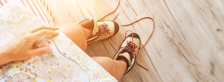 Young female inspecting a city map resting on the bed with untied trekking boots on wooden floorの写真素材
