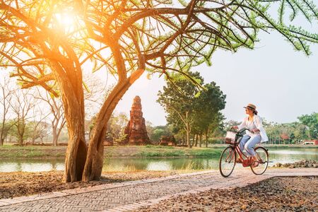 Female traveler wears light summer clothes and hat have early morning bicycle walk in Ayutthaya historical park, Thailandの写真素材
