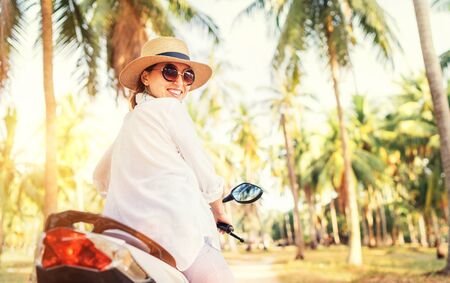 Happy smiling woman in straw hat and sunglasses riding motorbike under palm the trees	. Careless warm counries vacation time concept image.の写真素材
