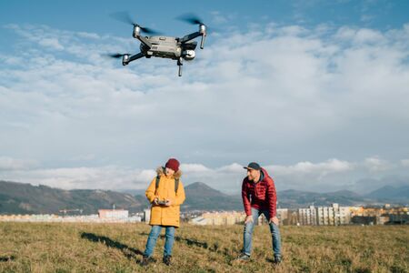 Father and Teenager boy son dressed yellow jacket piloting a modern digital drone using remote controller. Modern technology devises concept imageの写真素材