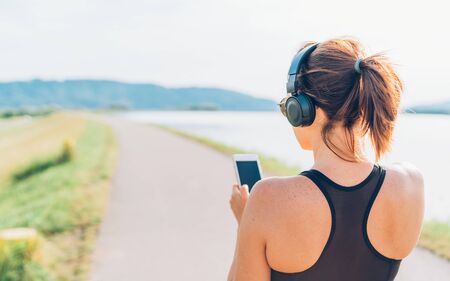 Young teenager girl starting jogging and listening to music using smartphone and wireless headphones.の写真素材