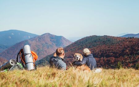 Father and son backpackers hikers resting on mountain hill and enjoying Low Tatras landscape with their beagle dogの写真素材