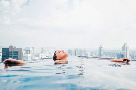 Young female relaxing in top roof infinity swimming pool with city view