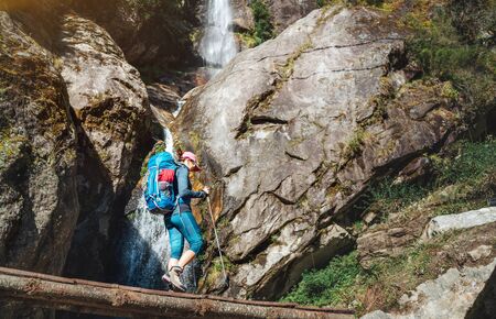 Young hiker backpacker woman using trekking poles hiking under the little waterfallの写真素材