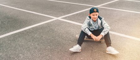 Teenager skateboarder boy with a skateboard sitting on asphalt playground and resting after he made tricks.の写真素材