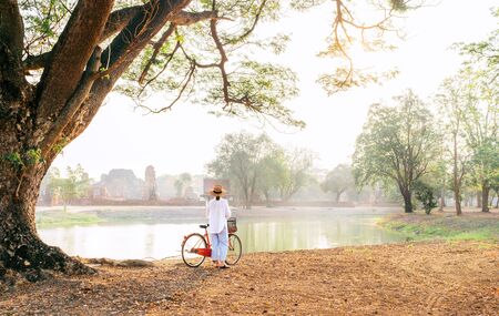 Young female traveler dressed light summer clothes and straw hat have early morning walk with bicycleの写真素材