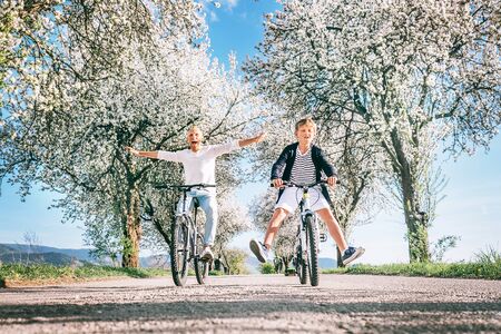 Father and son have a fun when riding bicycles on country road under the apple blossom trees. Free time spending with children concept image.の写真素材