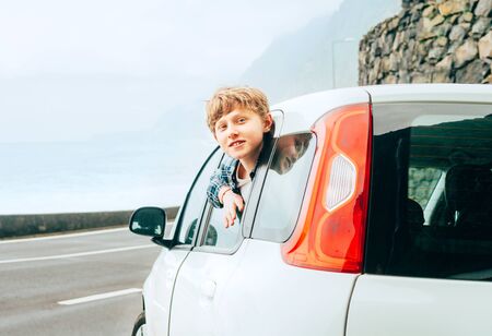 Blonde hair teenager boy look out from the rear passangers door of economy class auto and smiling.Rental car and Traveling by auto concept image.の写真素材