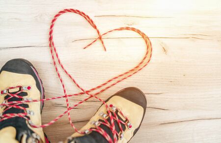 Conceptual image of the pair new trekking boots on the wooden floor background with released long shoelaces behind lying in heart shape.の写真素材