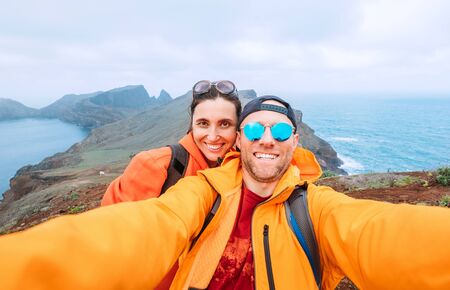 Smiling brightly dressed backpackers couple taking selfie portrait as they hiking and enjoying Atlantic ocean viewの写真素材