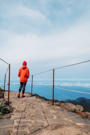 Young adult caucasian female dressed sporty clothes standing on the path and enjoying clouds view from Pico Ruivo mount 1861mの写真素材