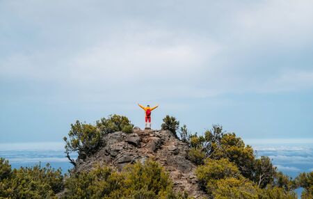 Young adult Caucasian man dressed  sporty clothes with red backpack rising up hands enjoying viewの写真素材
