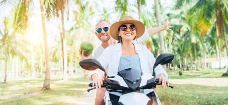 Happy smiling couple travelers riding motorbike scooter under palm trees.の写真素材