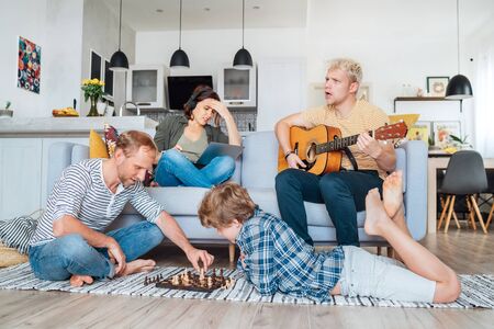 Family at living room together. Father playing chess with little son, mother learning online using...