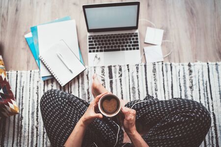 Business woman dressed pajamas enjoying morning coffee with heart shape foam sitting on living room floor office with laptopの写真素材