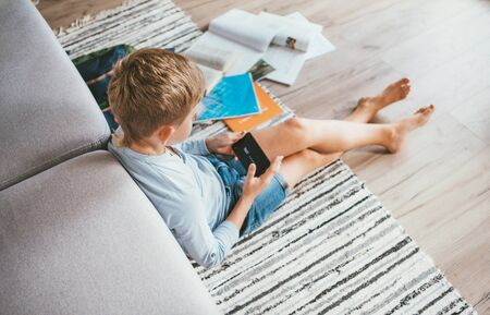 Preteen student boy using smartphone for distance online studying on a Global Coronavirus COVID-19 pandemic lockdown days.の写真素材