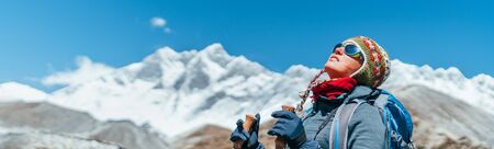 Young hiker backpacker female taking brake in hike walking during high altitude Everest Base Camp (EBC) route with snow Himalayan peaks on background.She using trekking poles. Active vacations conceptの写真素材
