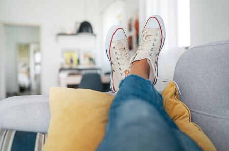 Young female lying in new beige sneaker son cozy comfortable living room sofa putting feet on...