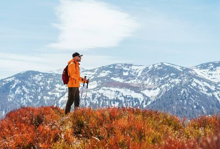 Dressed bright orange jacket backpacker walking by the touristic path using trekking poles in Mala...