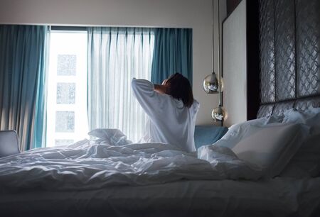Lazy female waking up in the morning. She stretching the body and looking in the window.
