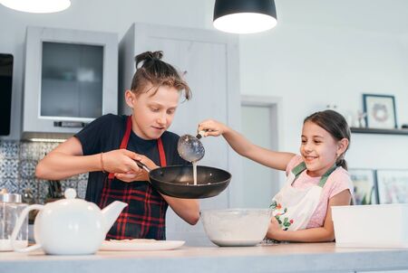 Sister and Brother dressed aprons making a homemade pancakes on the home kitchen.の写真素材