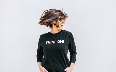Free feeling happy smiling woman posing in black sweatshirt with positive print Shine On. She rotating a head bacause a cheerful mood.の写真素材