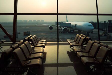 Waiting area with chairs in international airport terminal with behind a window aircraft flight preparation - fueling, catering, baggage services before airplane takeoff.の写真素材