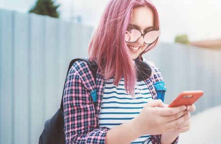Portrait of Beautiful modern young smiling female teenager with extraordinary hairstyle color in a checkered shirt browsing an internet via smartphone. Modern teens in digital world concept imageの写真素材