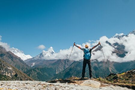 Active vacations concept image. Young hiker backpacker man rising arms with trekking poles enjoying the Thamserku 6608m mountain during high altitude Acclimatization walk. Everest Base Camp route,Nepal.の写真素材