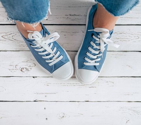 Teenager's feet in blue color casual new sneakers with white shoelaces on the white wooden floor close up image. Vintage style in modern fashion world concept image.の写真素材
