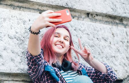Beautiful modern smiling young female teenager with extraordinary hairstyle color taking selfie or...