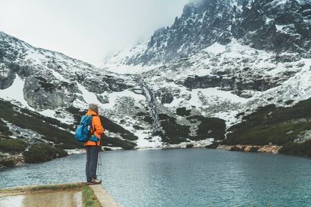 Dressed bright orange jacket female backpacker enjoying the Velicke pleso (mountain lake) view as she have mountain walk in Velicka valley in High Tatras, Slovakia. Active people in nature concept.の写真素材