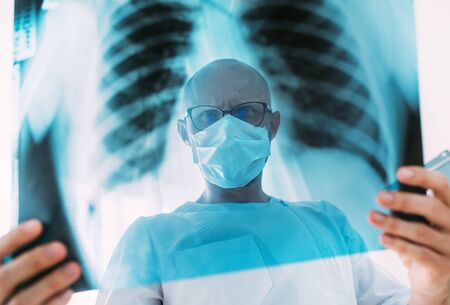 Male doctor portrait throught the patient chest x-ray film lungs scan at radiology department in...