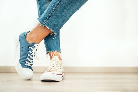 Teenager's feet posing in casual different colors beige and blue new sneakers on the white wooden floor close up image. Vintage style in modern fashion world concept image.の写真素材