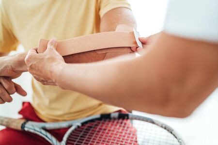 Tennis player elbow taped with elastic therapeutic or Kinesio tape applied by nurse at orthopedic ward close up image. Active sporty people health rehabilitation concept image.の写真素材