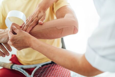 Tennis player elbow taped with elastic therapeutic or Kinesio tape applied by nurse at orthopedic ward close up image. Active sporty people health rehabilitation concept image.の写真素材