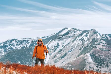 Dressed bright orange jacket backpacker walking by red blueberry field using trekking poles with mountain range background, Slovakia. Active people and European mountain hiking tourism concept image.の写真素材
