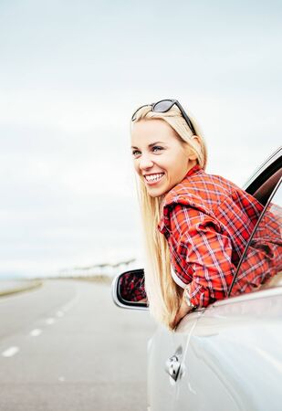 Happy smiling young woman looks out from car windowの写真素材