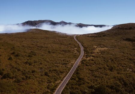 Country asphalt road ER209 leading to clouds stuck at mountain hills in the inland of Madeira island, Portugal aerial drone shot. Traveling and transportation concept image.の写真素材