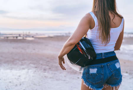 Young long haired woman dressed sexy jeans shorts making moto trip rest with motorcycle helmet enjoying a sunset sky on Koh Samui island, Thailand. Traveling in exotic countries concept image.の写真素材