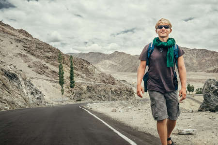 Traveler young man walking by the mountain road in Indian Himalaya mountains. Traveling around the world concept image.の写真素材