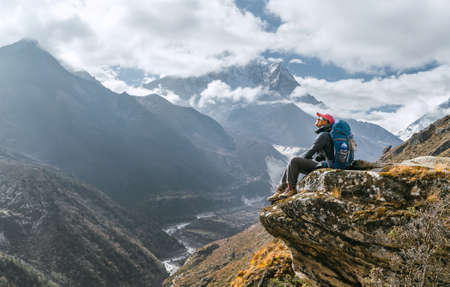 Young hiker female backpacker sitting on the cliff edge and enjoying mountain peaks view during Everest Base Camp (EBC) trekking route near Phortse, Nepal. Active vacations image conceptの写真素材