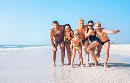 Three family generations on the one long shoot posing for group photo on the beach. Kids, teenagers, Parents and Grandparents together traveling concept image.