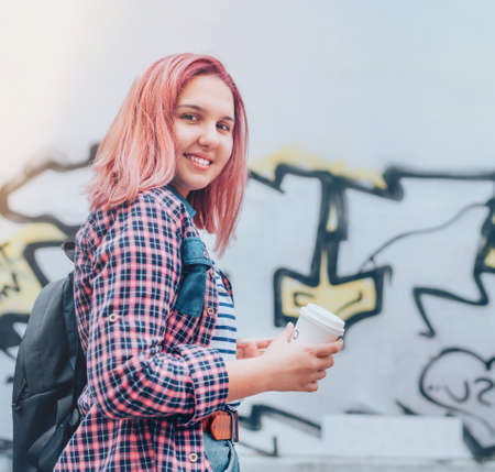 Cheerfully smiling Beautiful modern young female teenager Portrait with extraordinary hairstyle color in checkered shirt holding "coffee to go" cap.  Modern teens or cheerful students concept imageの写真素材